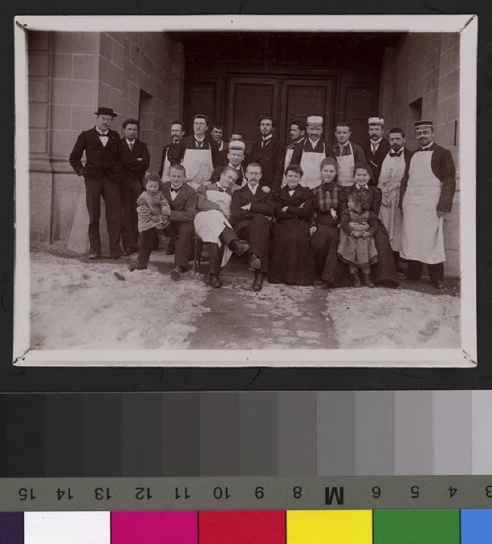 Volée d'étudiants avec leurs professeurs sous le porche de l'Ecole de médecine. On reconnaît, a gauche de l'image, les mains dans les poches et chapeau sur la tête, le professeur Henri Preisig. Quelques portraiturés portent la casquette de leur société…