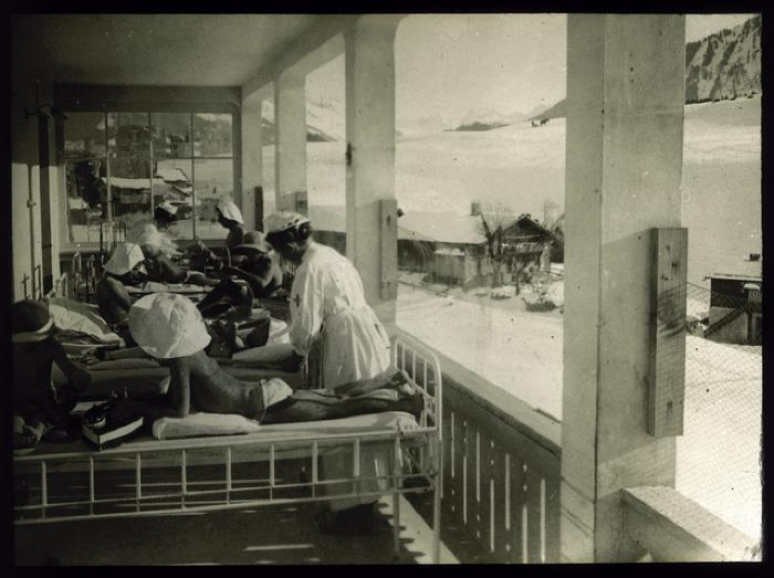 Enfants allités en cure de soleil et d'air pur sur une véranda. Des infirmières prennent soin d'eux.